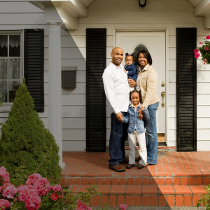 Smiling family standing on the front porch of their new home, symbolizing the joy of having a place to call their own.
